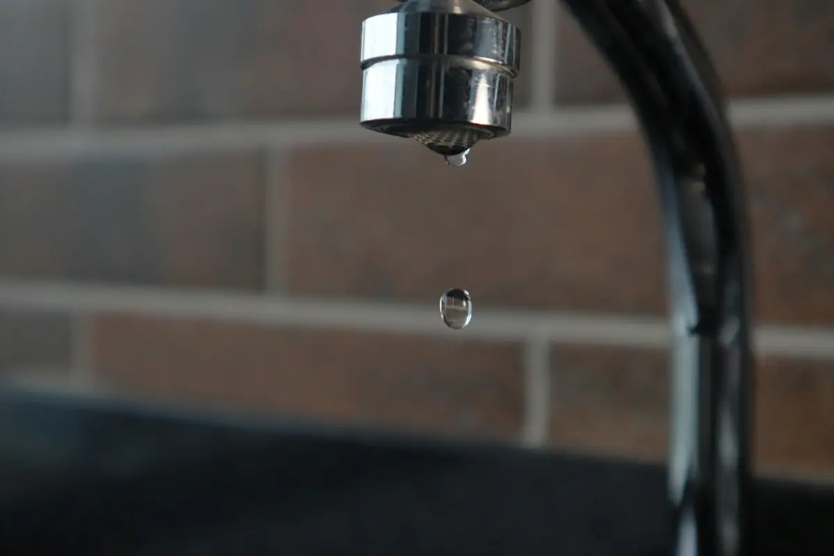 A chrome tap dripping, against a brick wall
