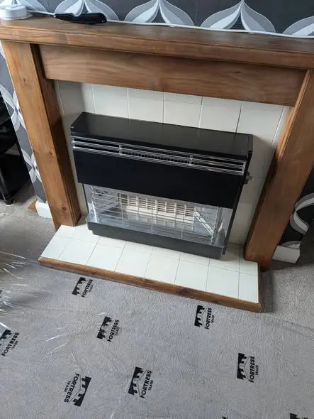A new black gas fire fitted in a wooden fireplace surround with a white tiled hearth, dust sheets protecting the carpet
